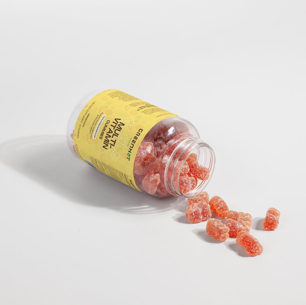 A toppled bottle of GreenHat's Multivitamin Bear Gummies spills orange gummies on a white surface, with a yellow label suggesting essential nutrients to support your immune system.