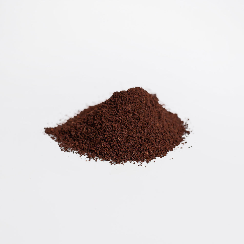 A small mound of finely ground Organic Hemp Coffee Blend by GreenHat is scattered on a white surface.