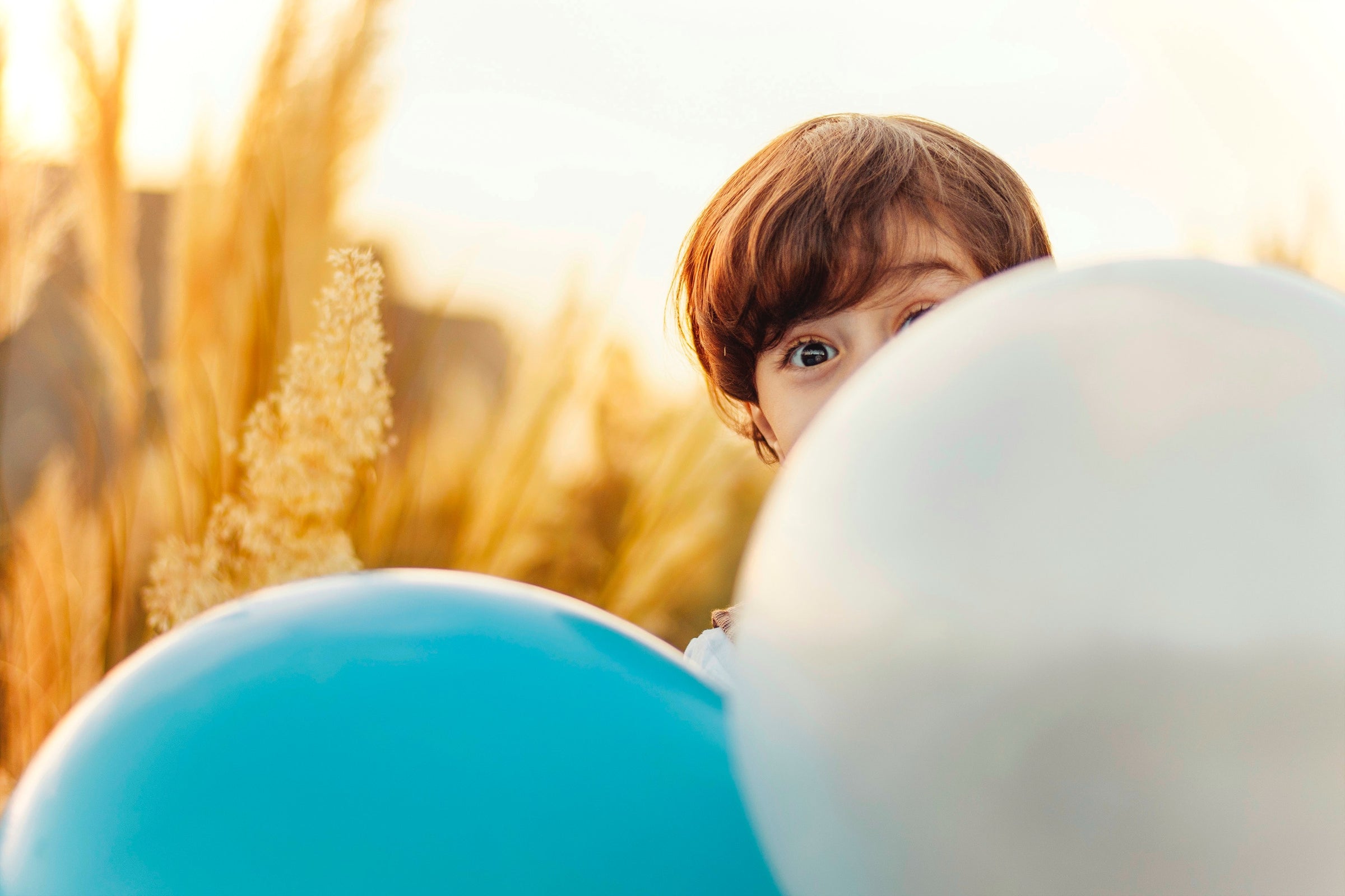 little boy hiding behind blue and white ballon