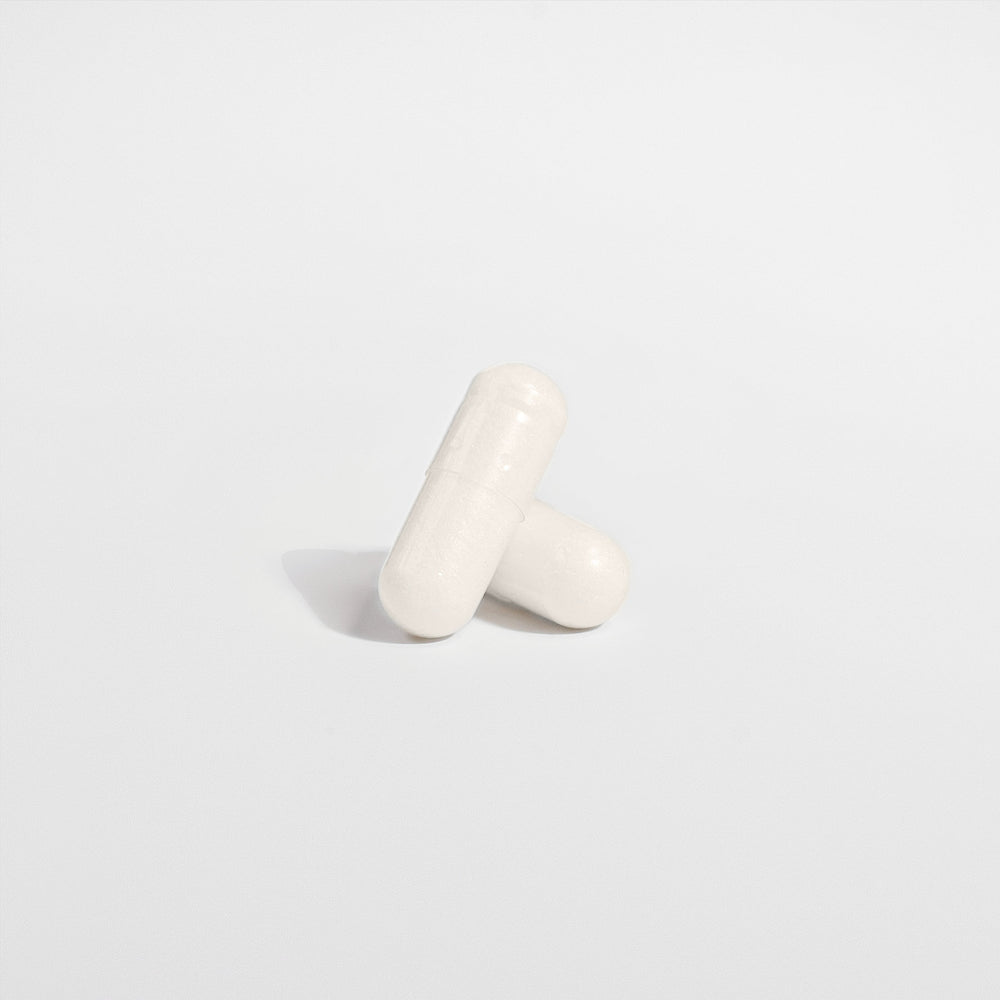 Two white, oblong capsules, one leaning against the other on a plain, light-colored background, highlight the serenity brought by GreenHat's 5-HTP - Serotonin Enhancer supplement known for its mood enhancement properties.
