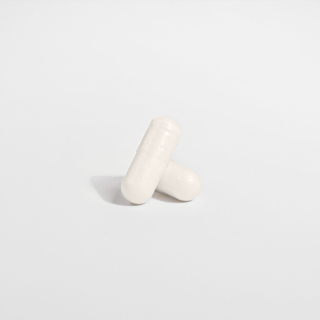 Two white, oblong capsules, one leaning against the other on a plain, light-colored background, highlight the serenity brought by GreenHat's 5-HTP - Serotonin Enhancer supplement known for its mood enhancement properties.