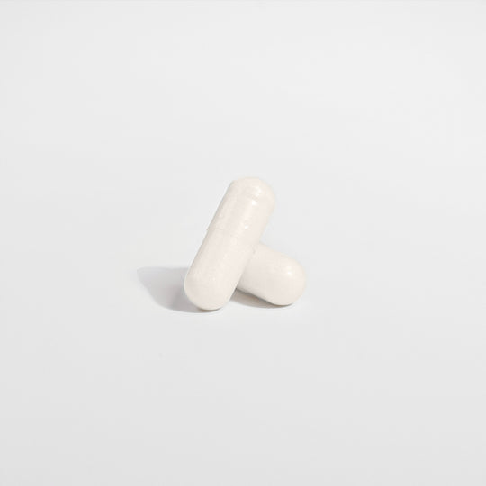 Two white, oblong capsules, one leaning against the other on a plain, light-colored background, highlight the serenity brought by GreenHat's 5-HTP - Serotonin Enhancer supplement known for its mood enhancement properties.