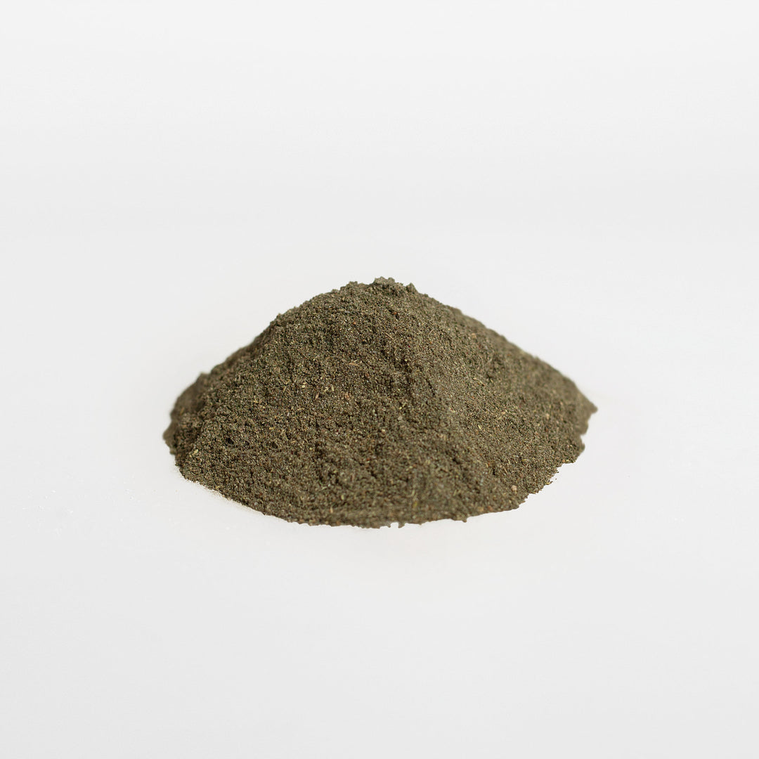 A small mound of finely ground, dark green Ultra Clean Smoothie Greens - Natures Best by GreenHat against a plain white background.