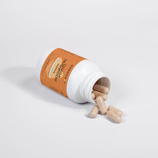 A white bottle with an orange label tipped over, spilling beige capsules onto a white surface. The label reads "Chaga Mushroom - Natural Immunity" and highlights a combination of multiple medicinal mushrooms, including immune-boosting Chaga mushroom by GreenHat.