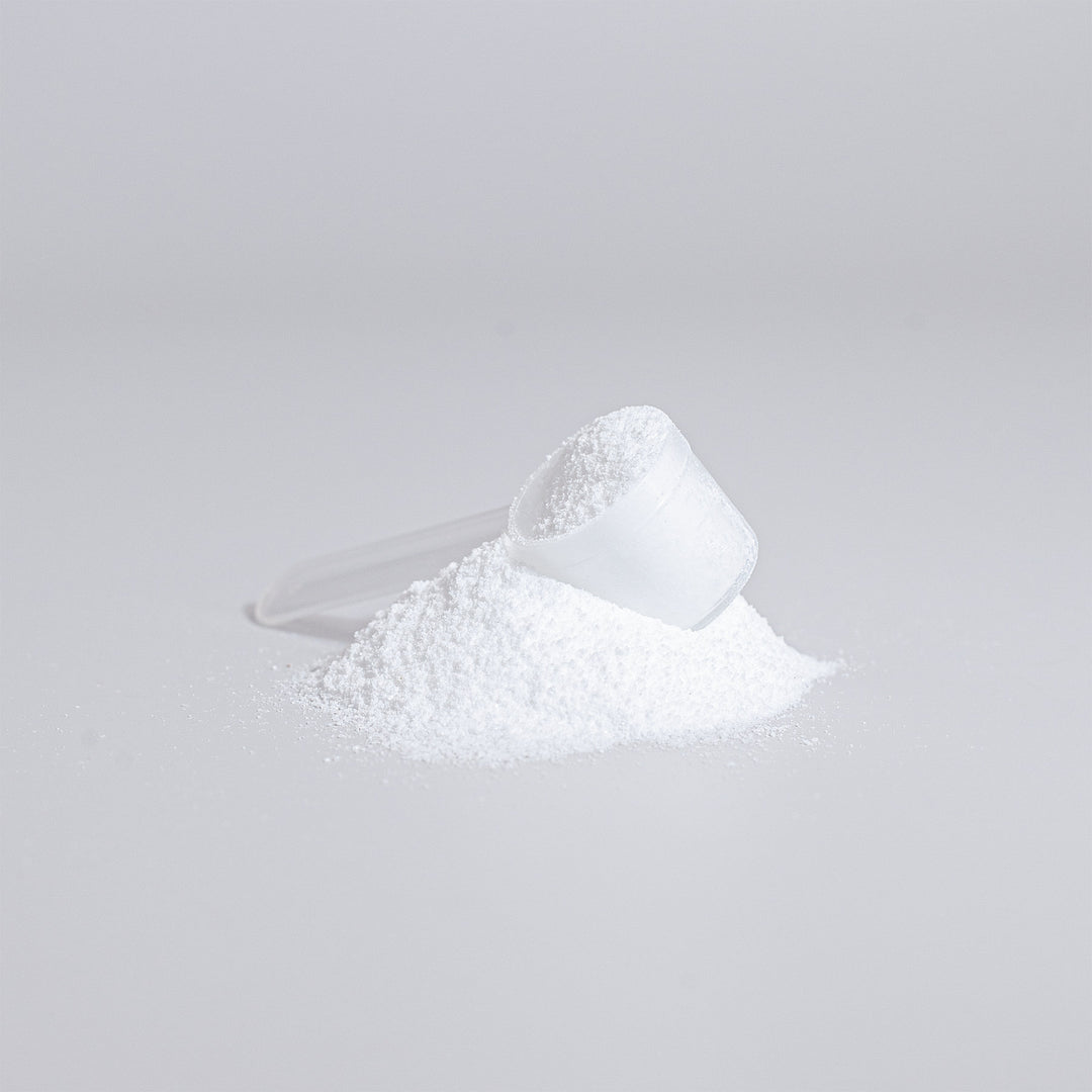 A plastic scoop is filled with white powder, placed on top of a small heap of Creatine Monohydrate - Enhance Strength & Performance by GreenHat, ready to boost athletic performance against a white background.