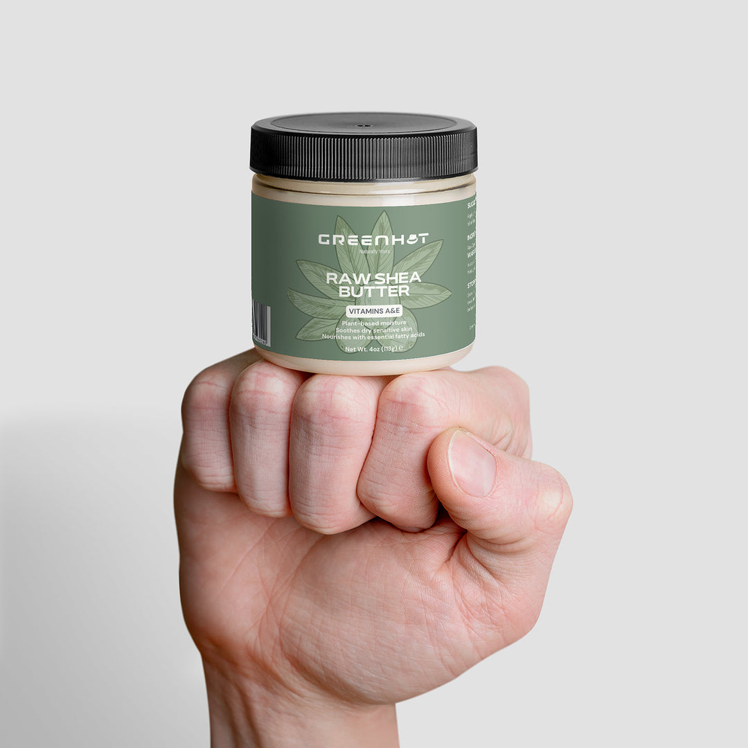 A hand is holding a jar of GreenHat Raw Shea Butter, showcasing its unrefined goodness against a white background.