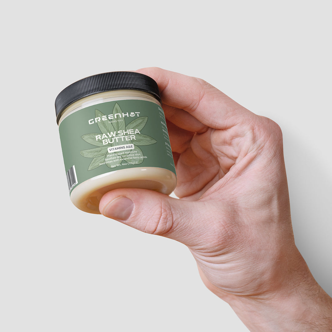 Hand holding a jar of GreenHat Raw Shea Butter. The label highlights Vitamins A, C, E and features an image of a shea nut, emphasizing the unrefined goodness of this plant-based moisturizer.