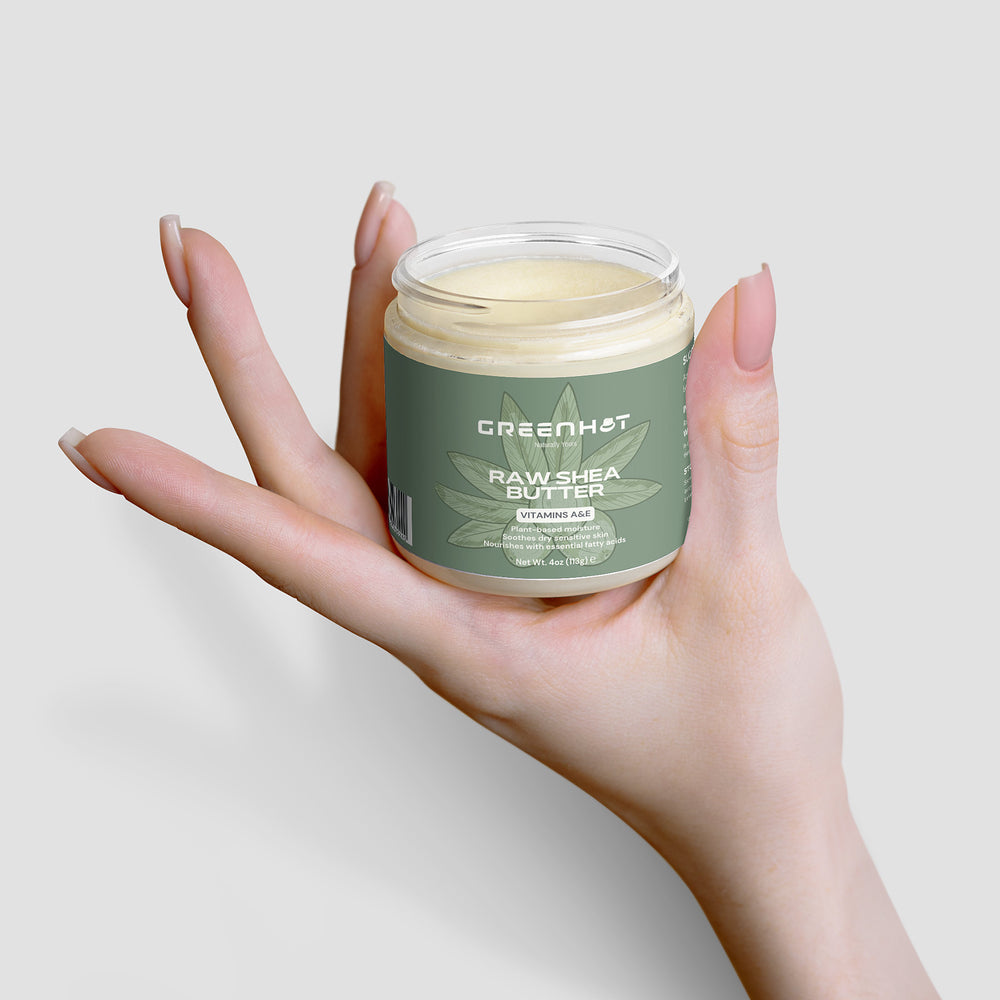 A person with long nails holds a small jar of GreenHat Raw Shea Butter, showcasing unrefined goodness.