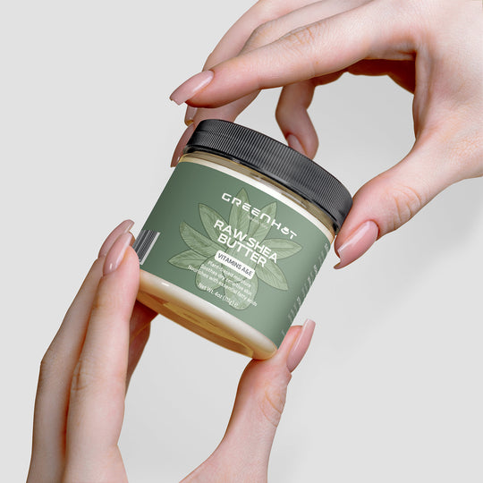 A hand holding a jar of "GreenHat Raw Shea Butter," an organic, plant-based moisturizer with a green label displaying the product name and "Vitamin A & E.