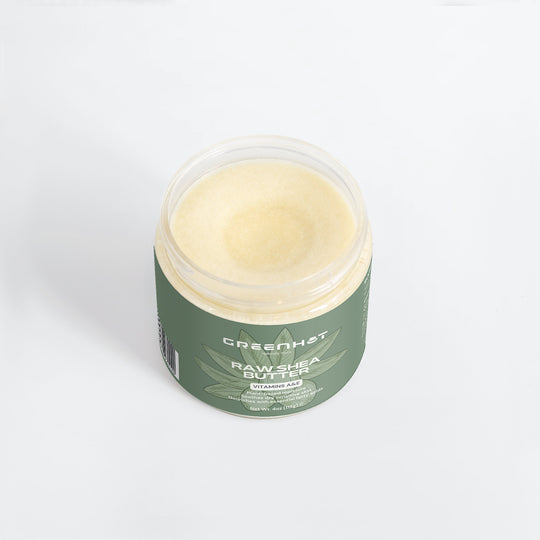 A jar of GreenHat Raw Shea Butter with vitamin E, amino acids, and keratin. The jar is green with a white lid and contains solid yellowish shea butter rich in unrefined goodness.