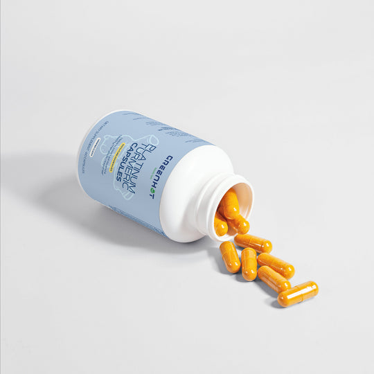 A plastic bottle labeled "Platinum Turmeric - Immunity Accelerator" by GreenHat lies on its side, with several yellow capsules spilling out onto a white surface. This blend of natural ingredients offers both joint pain relief and enhanced digestive health.