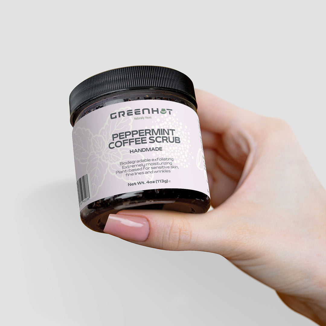 A hand with painted nails holds a jar of GreenHat Peppermint Coffee Scrub, labeled as handmade, biodegradable, and 4 oz (113g). Enjoy the antioxidant-rich coffee for effective exfoliation.