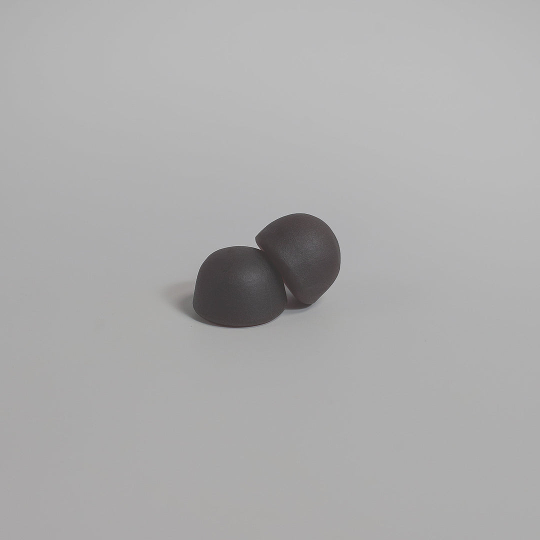 Two small, black, dome-shaped objects resting on a plain white surface, reminiscent of GreenHat Mushroom Extract Complex Gummies to boost your immunity.