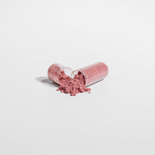 An open capsule with pink powder, rich in beetroot antioxidants, spilling out on a white background. GreenHat's Beetroot - Natural Energy Booster.