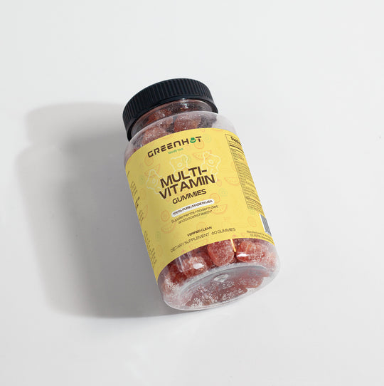 A plastic bottle labeled "GreenHat Multivitamin Bear Gummies - Daily Nutritional Needs" contains red gummy vitamins. The yellow label features nutritional information and highlights essential nutrients for the immune system. Topped with a black cap, the bottle is partially full.