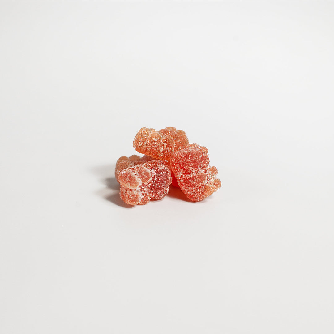 A close-up image of several sugar-coated orange Multivitamin Bear Gummies - Daily Nutritional Needs by GreenHat piled on a white surface, providing essential nutrients to support your immune system.