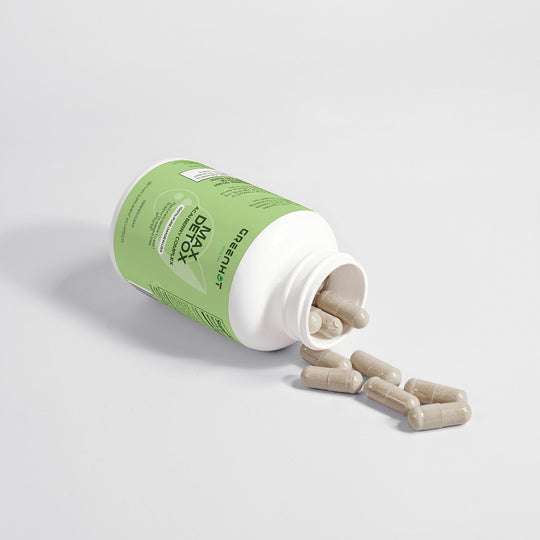 A white bottle with a green label is tipped over, spilling several beige capsules onto a smooth white surface, perfect for kickstarting your Max Detox (Acai detox) - Detoxifying Cleanse by GreenHat.