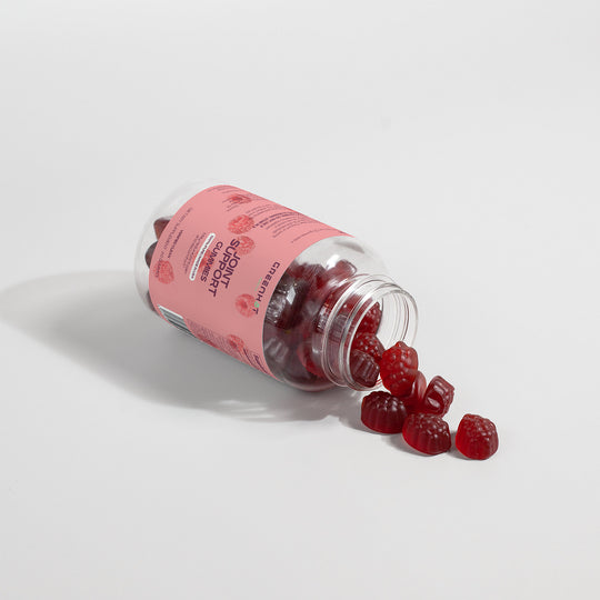 A plastic bottle of GreenHat Joint Support Gummies (Adult) lies on its side with several gummies spilled out. The label on the bottle is pink, highlighting their glucosamine content to help alleviate joint discomfort.