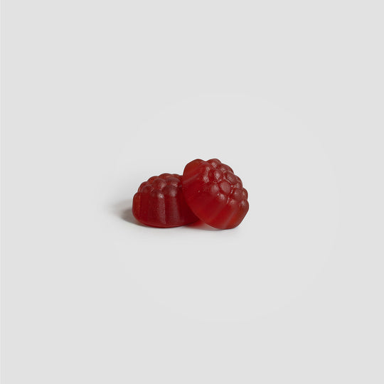 Two red gummy candies shaped like raspberries are placed against a plain gray background, resembling delicious Joint Support Gummies (Adult) by GreenHat designed to aid with joint discomfort.