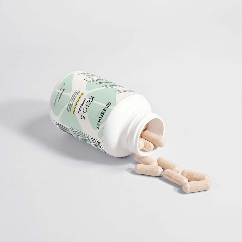 A white bottle labeled "GreenHat Keto-5 - Unlimited Energy" with beige capsules partially spilled out on a white surface, designed for ultimate keto support and enhanced fat burning.