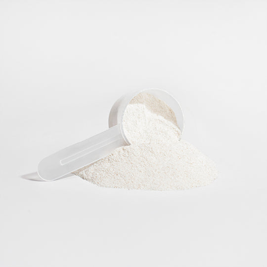 A white scoop partially buried in a pile of fine, white GreenHat grass-fed collagen creamer (Vanilla) on a plain background.