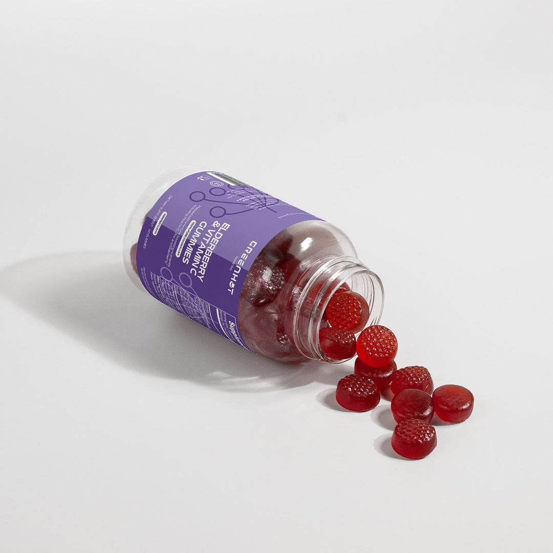 A bottle of GreenHat Elderberry & Vitamin C Gummies tipped over with red gummies spilled out on a white surface.