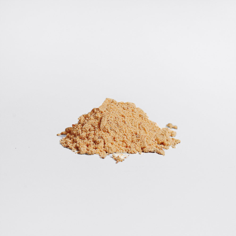 A small pile of light brown powder, known as Bee Pearl Powder - Superfood Powerhouse by GreenHat, rests gently on a white surface, promoting holistic well-being and radiant skin.