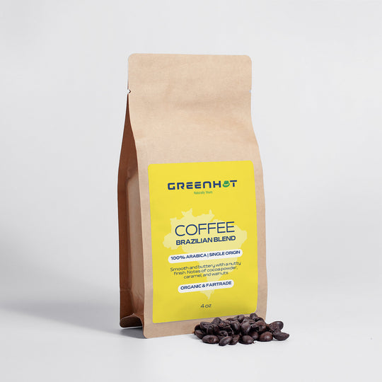 A brown paper coffee bag labeled "GreenHat" with text for Brazilian Blend 4oz - 100% Arabica, and a yellow label, stands beside scattered Arabica coffee beans on a white surface.