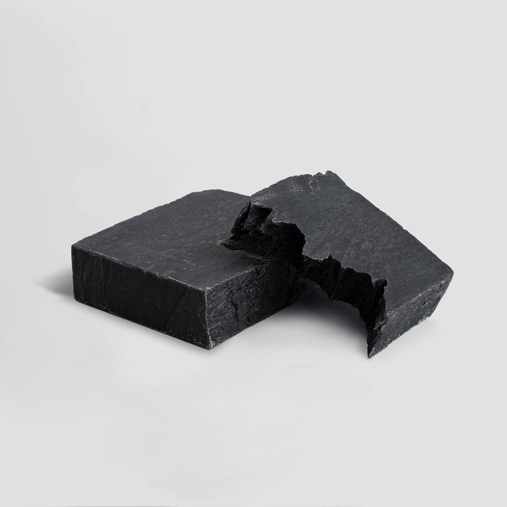 Two pieces of a broken GreenHat Charcoal Detox Soap against a plain white background.