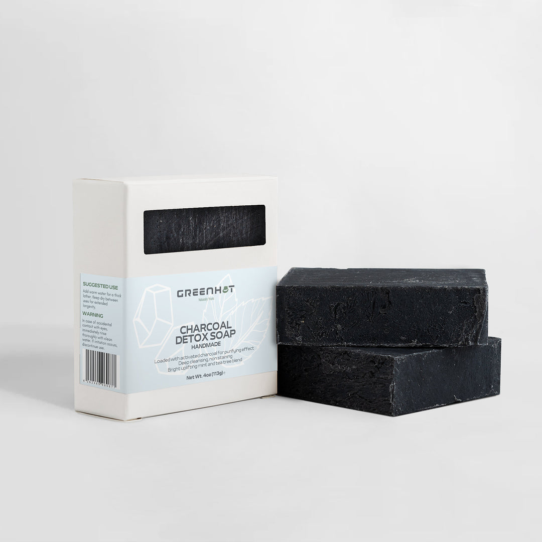 A box of GreenHat Charcoal Detox Soap next to two black Activated Charcoal soap bars on a white background.