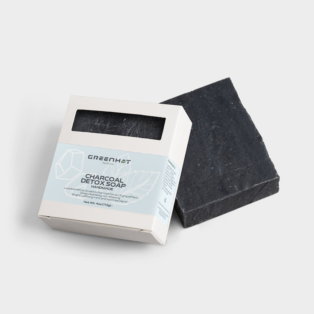 A Charcoal Detox Soap by GreenHat lying next to its open packaging on a white background.