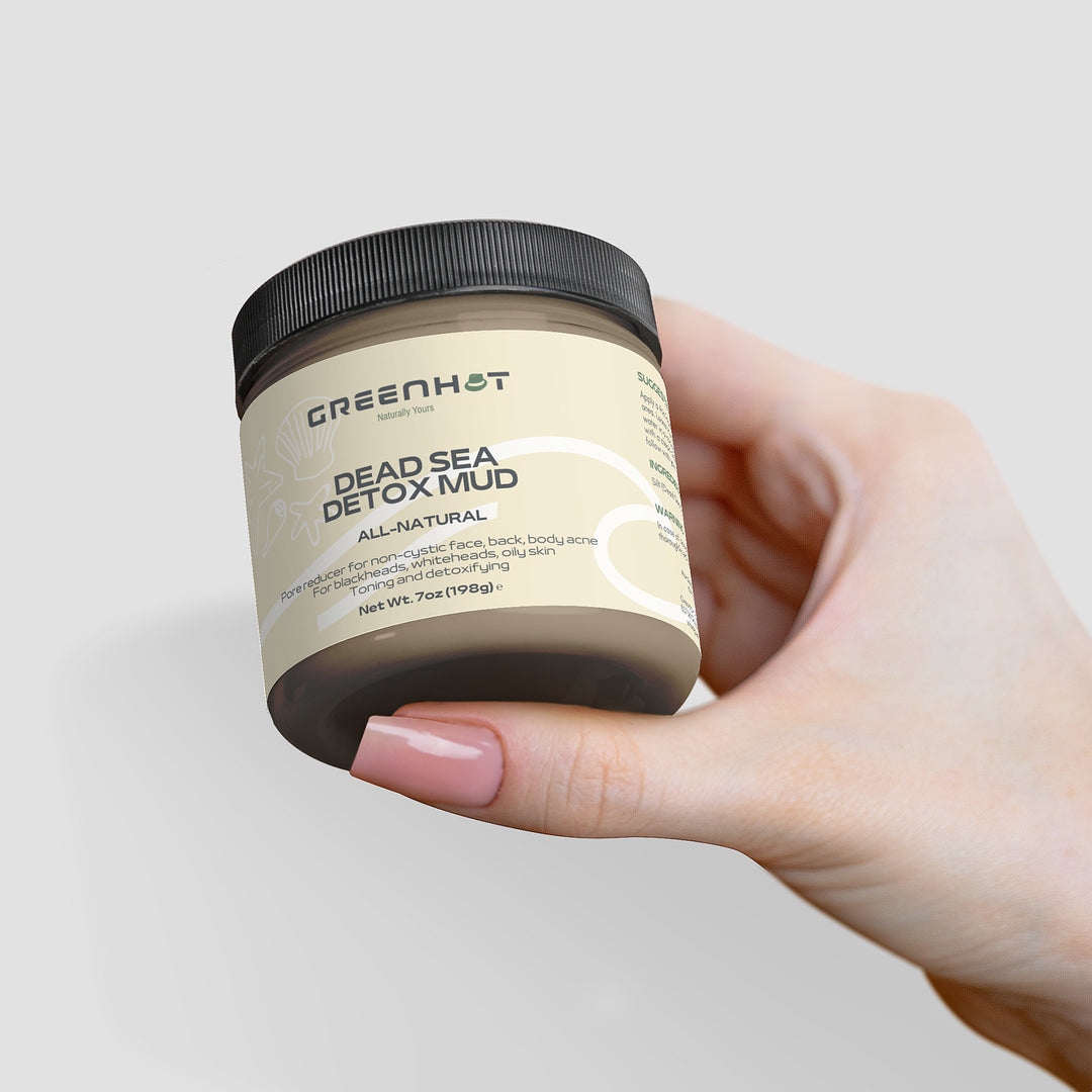 A hand holding a jar of GreenHat Dead Sea Detox Mud labeled for natural skincare and body use, against a light gray background.