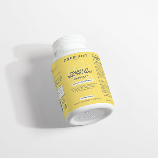 A yellow and white bottle of GreenHat Complete Multivitamin, enriched with immune-boosting herbs and antioxidants, contains 60 vegetable capsules. The bottle is standing on a white surface.