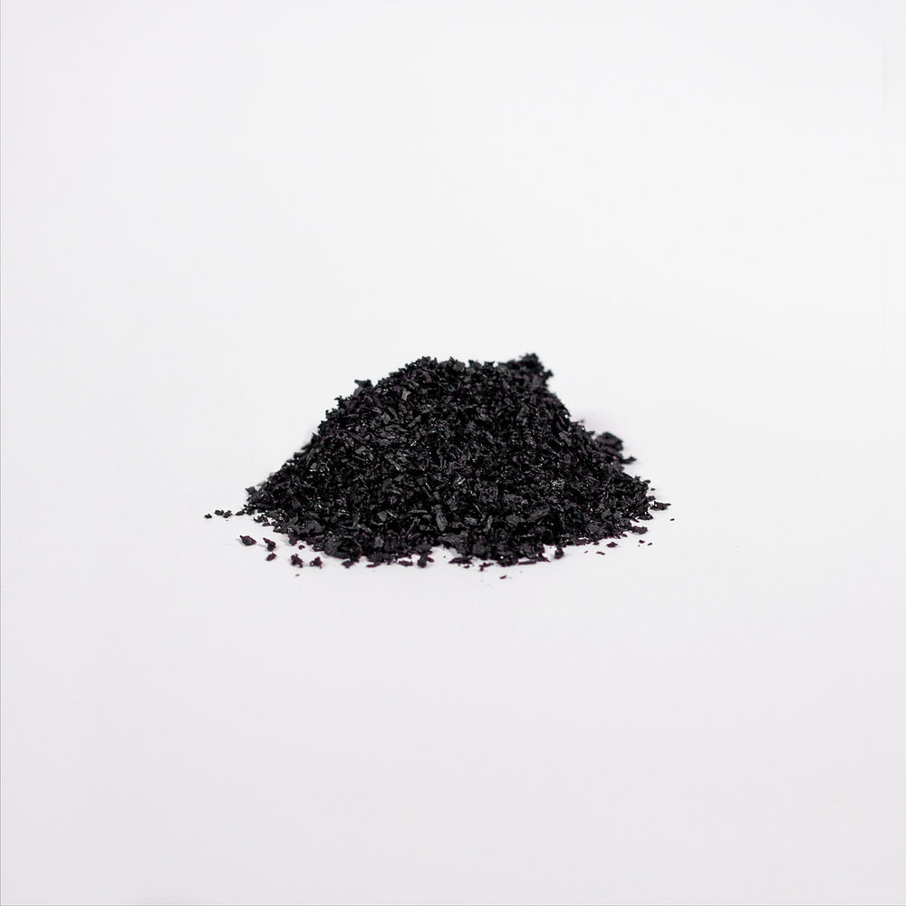 A pile of coarse black granules, rich in Birch Chaga Microbiome Wellness Powder by GreenHat, sits on a smooth white surface.