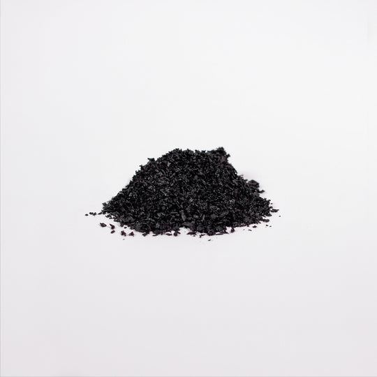 A pile of coarse black granules, rich in Birch Chaga Microbiome Wellness Powder by GreenHat, sits on a smooth white surface.