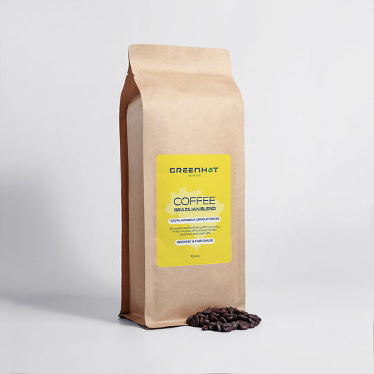 A Brazilian Blend 16oz GreenHat coffee bag with a yellow label, indicating it contains single origin 100% Arabica coffee beans, positioned upright on a grey background, accentuated by some scattered coffee beans at the front.