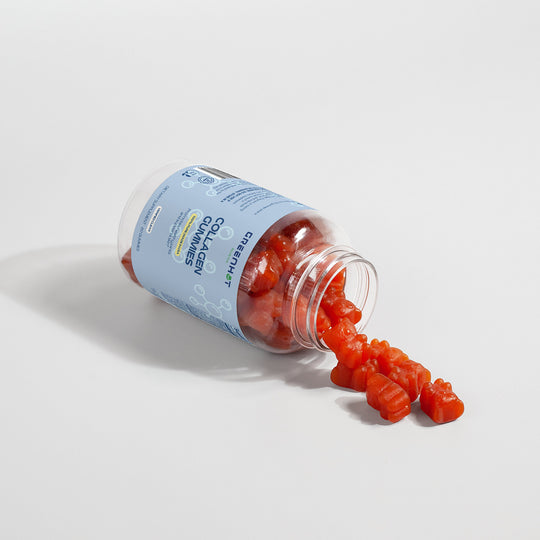 A bottle of GreenHat Collagen Gummies enriched with Vitamin C lies on its side, spilling several red gummy bears. The label on the beauty nourishment supplement is blue and partially visible.