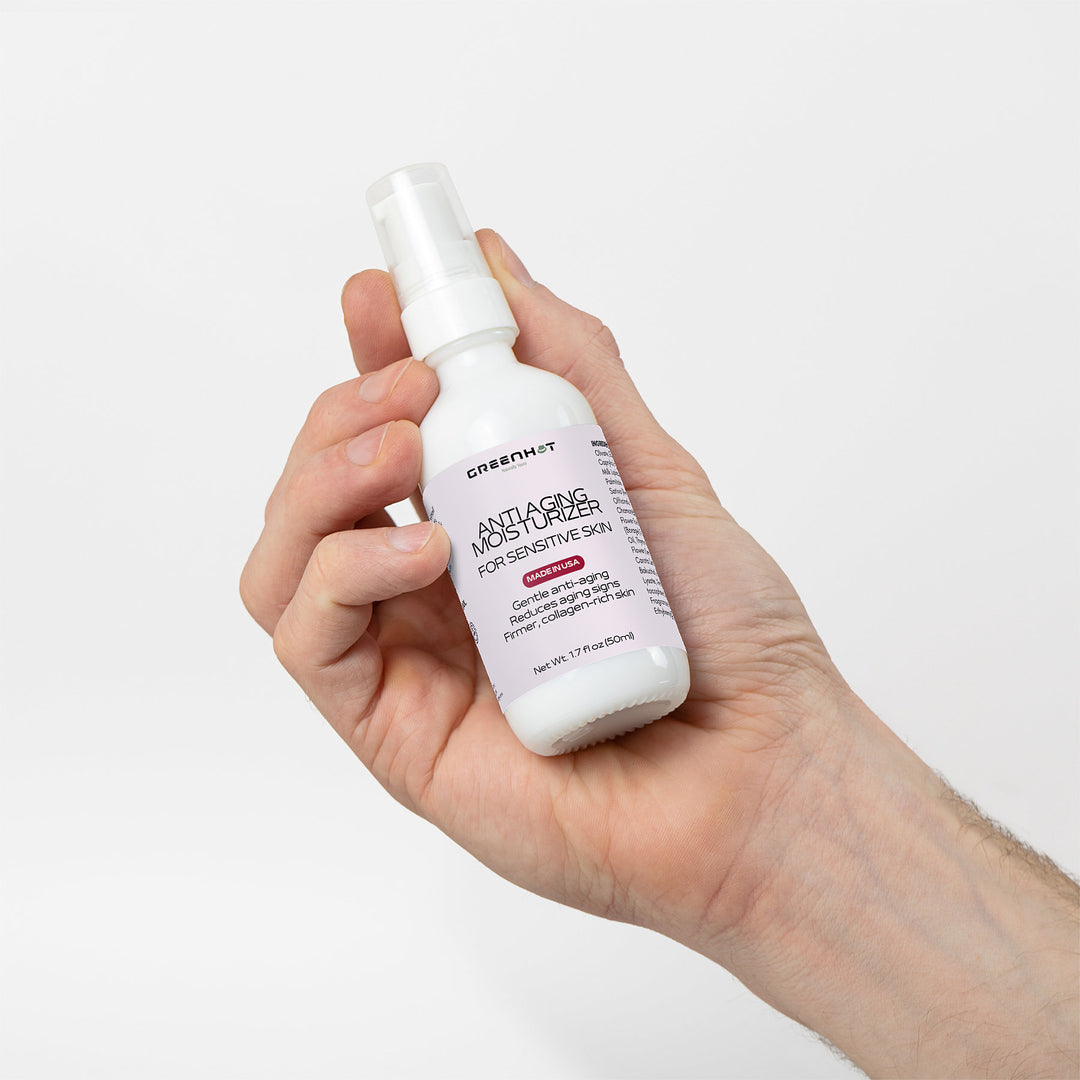 A hand holding a bottle of GreenHat Anti Aging Moisturizer for Sensitive Skin, ideal for sensitive skin, against a white background.