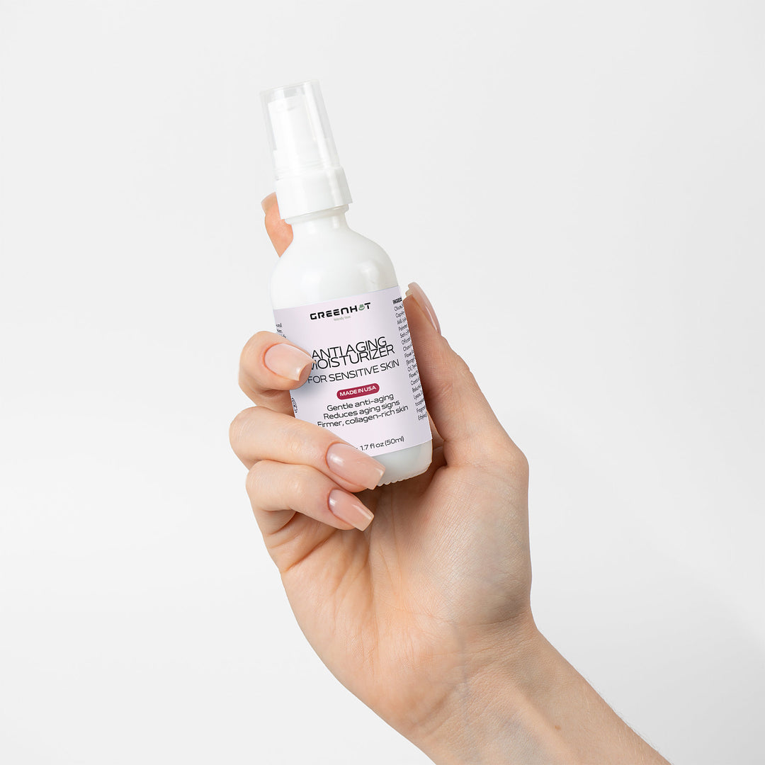 A hand holding a bottle of GreenHat Anti Aging Moisturizer for Sensitive Skin against a white background.