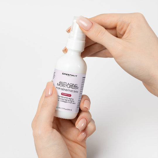 A person holding a bottle of GreenHat Anti Aging Moisturizer for Sensitive Skin against a white background.