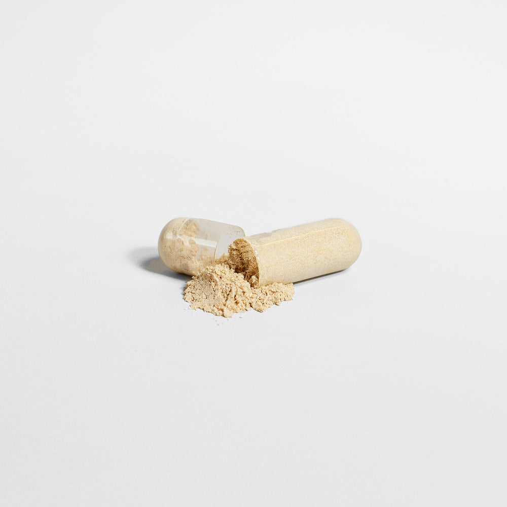 A broken open capsule filled with GreenHat's Ashwagandha - Unlock Your Inner Energy powder spilled out on a plain white background.