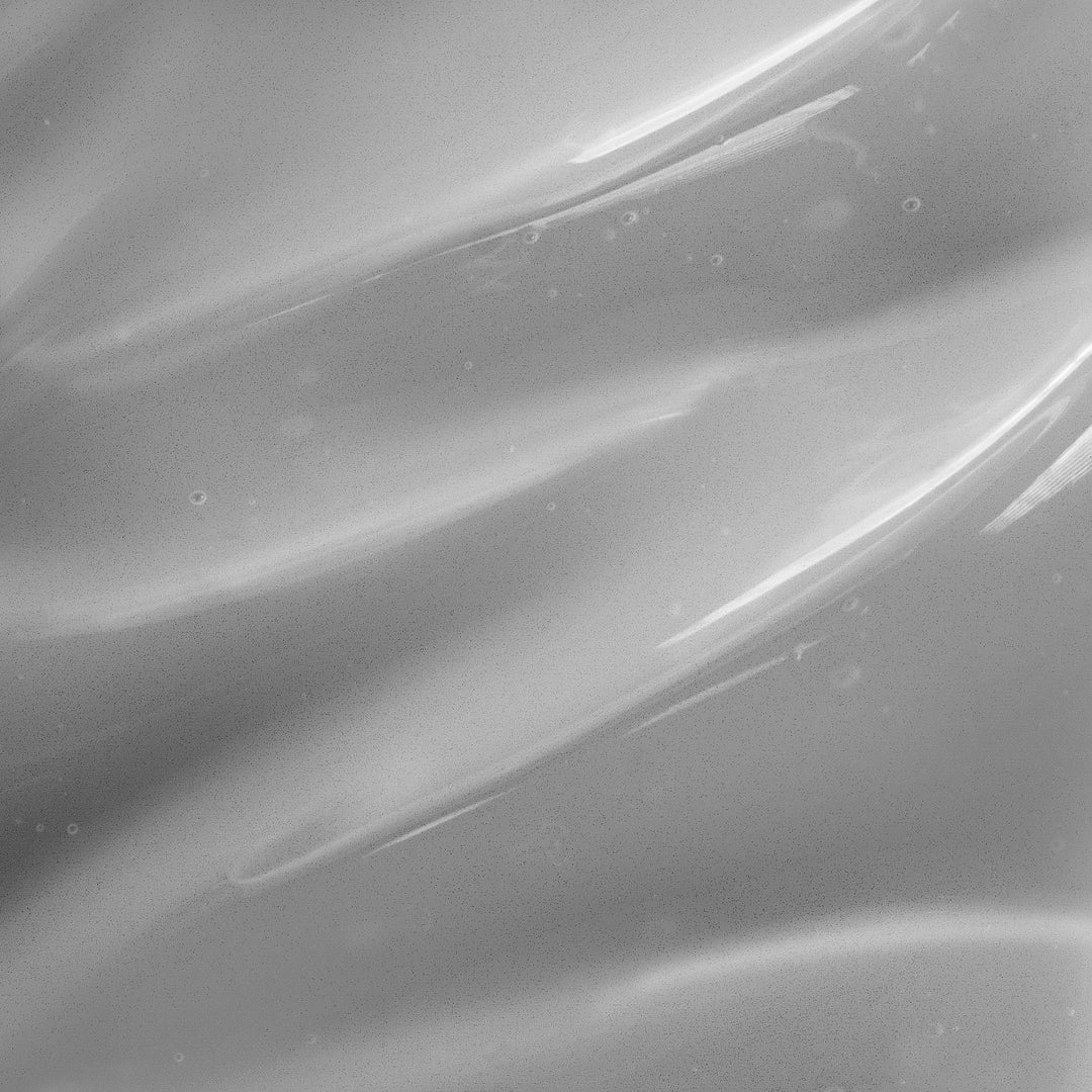 Close-up view of a smooth, monochromatic surface with flowing, wavy patterns and minute specks scattered across, evoking the look of a high-quality Charcoal Facial Cleanser by GreenHat made for daily use.