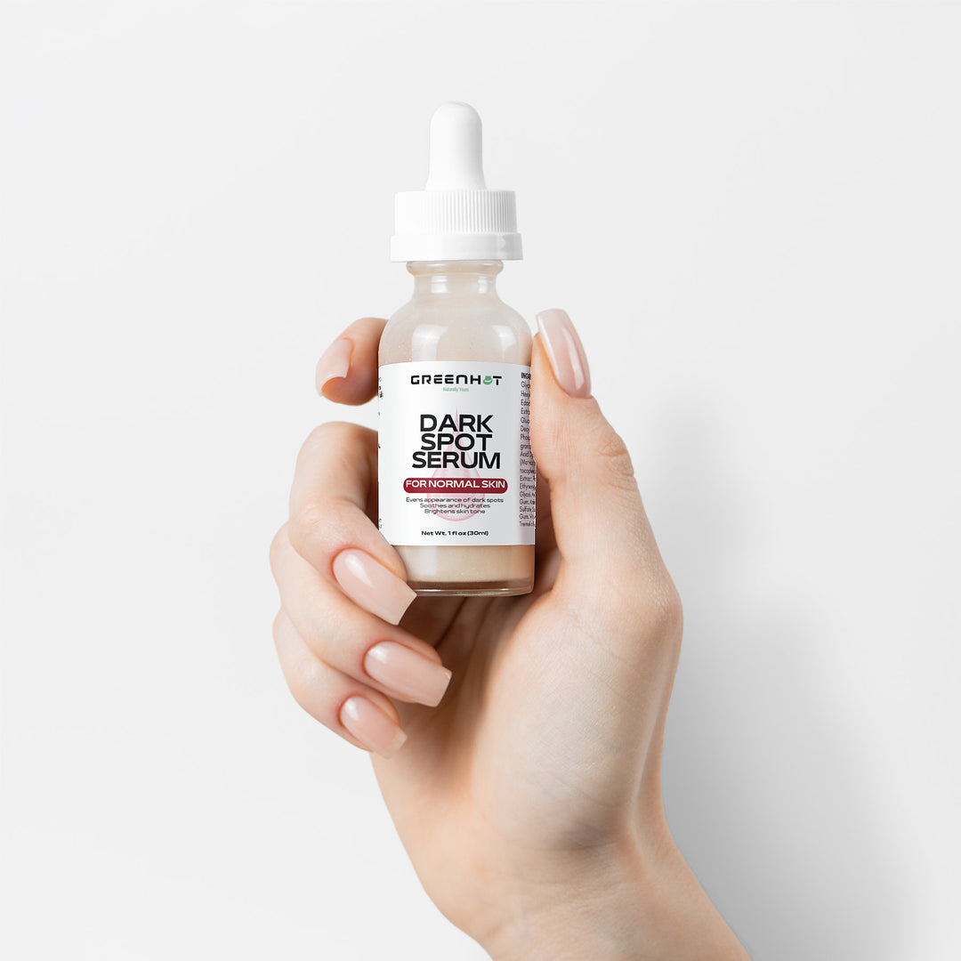 A hand holding a small bottle of GreenHat Dark Spot Serum for Normal Skin with a dropper cap and a label that reads "Paraben Free," ideal for achieving an even skin tone.