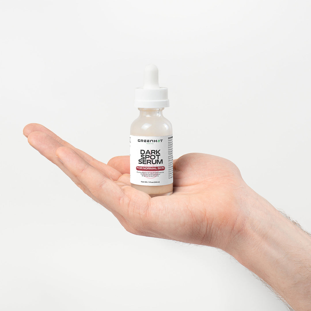 A hand holds a small bottle labeled "Dark Spot Serum for Normal Skin" by GreenHat against a plain white background, promising dark spot reduction for an even skin tone.