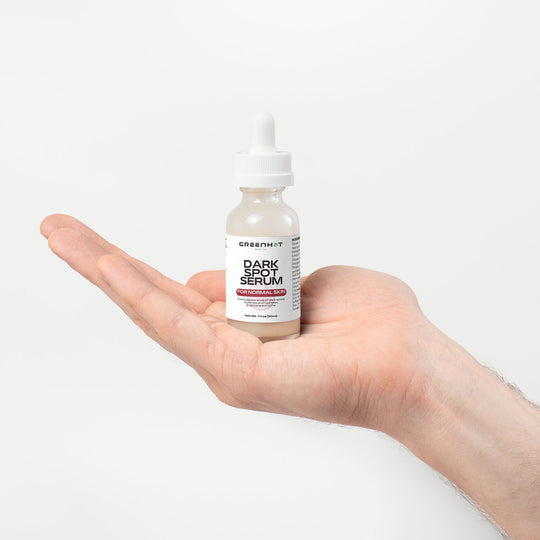 A hand holds a small bottle labeled "Dark Spot Serum for Normal Skin" by GreenHat against a plain white background, promising dark spot reduction for an even skin tone.