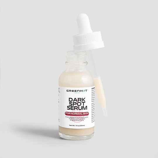 A bottle of dark spot serum labeled "GreenHat Dark Spot Serum for Normal Skin" with an off-white liquid inside. The cap is a dropper resting beside the bottle, which holds the text and ingredient information, promising effective dark spot reduction for an even skin tone.