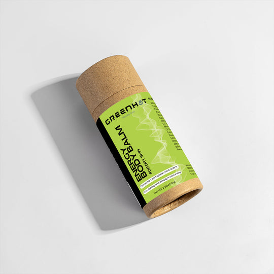 A cylindrical cardboard tube labeled "GreenHat Energy Body Balm" lies on its side against a white background. The eco-friendly label features green and black colors with text and a graphic design element, promoting this moisturizing treatment.