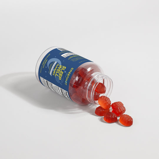 A bottle labeled "GreenHat Sleep Well Gummies (Adult)" lies on its side with red gummies spilling out on a white surface, promising restful nights as a natural sleep aid.