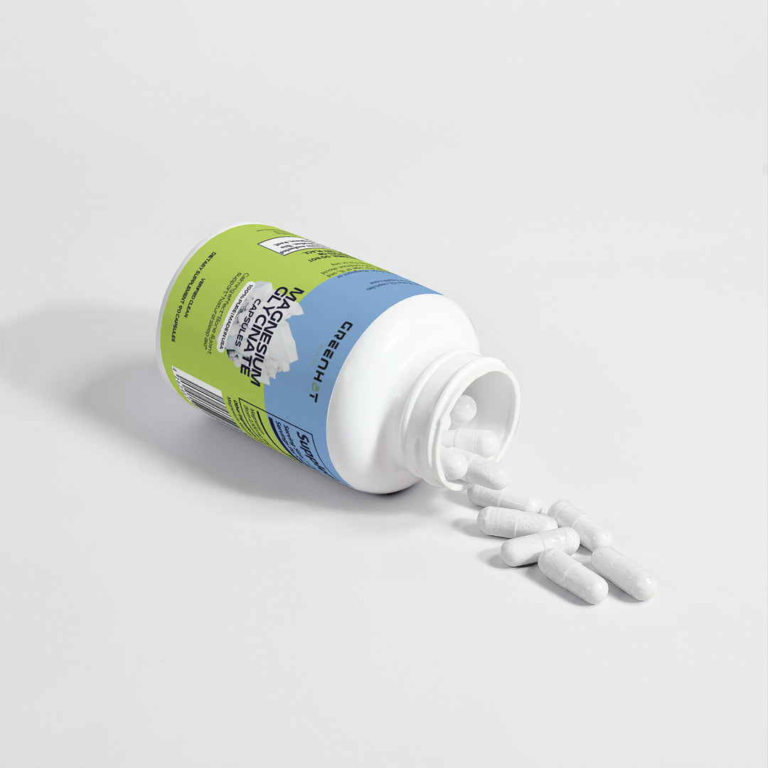 An open GreenHat "Magnesium Glycinate" bottle tips on its side, spilling white capsules onto a white surface. These supplements help address magnesium deficiency and support overall well-being.