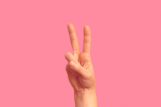 A hand is shown against a pink background, with the index and middle fingers raised, forming a "V" shape—a subtle nod to mood elevation, thanks to 5-HTP - Double Pack by GreenHat.